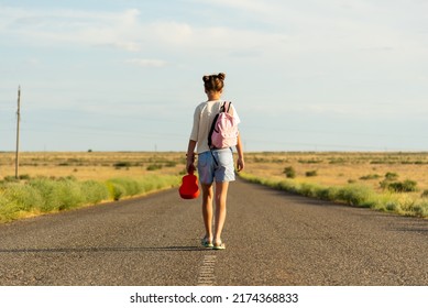 A girl walks along an empty road in the steppe. She has a ukulele in her hands and a backpack on her shoulders. It's summer and warm outside. Open road.