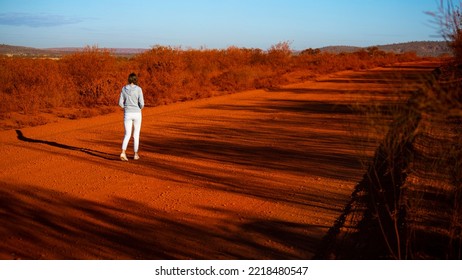 Girl Walks Along Red Dirt Road In Karijini National Park In Western Australia, Girl Lost In Middle Of Desert In Australian Outback