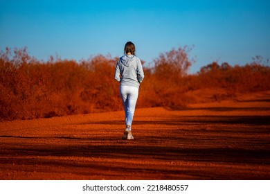 Girl Walks Along Red Dirt Road In Karijini National Park In Western Australia, Girl Lost In Middle Of Desert In Australian Outback