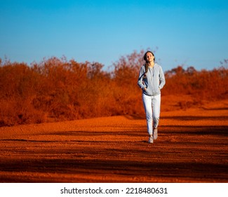 Girl Walks Along Red Dirt Road In Karijini National Park In Western Australia, Girl Lost In Middle Of Desert In Australian Outback