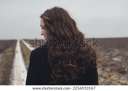 A girl walks along the road. A woman with long curly hair. Emotions of sadness and longing. A lonely girl walks. A woman walks alone. Thinks and dreams. A lonely woman in the field.The wind blows.