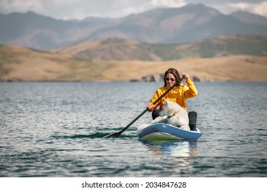 Girl Walks On Stand Up Paddle Board At Mountain Lake With White Siberian Dog. Travel Concept