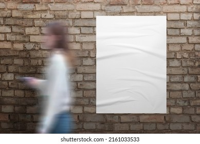 Girl walks past a white poster on brick street wall. Blank white poster with crumpled texture for design presentation