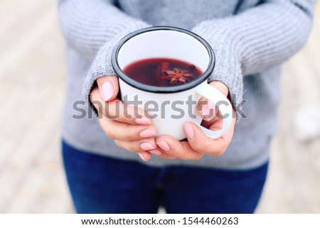 Girl in warm wool light sweater is holding metal mug with mulled wine. Warm autumn day, soft sunlight, bright colors. Cinnamon and anise for rich taste of hot spicy beverage. Cozy mood