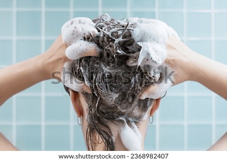 Girl washes her hair with shampoo on blue background, back view