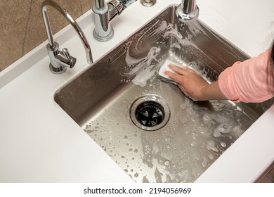 Girl washing a steel sink with a sponge and foam in the kitchen