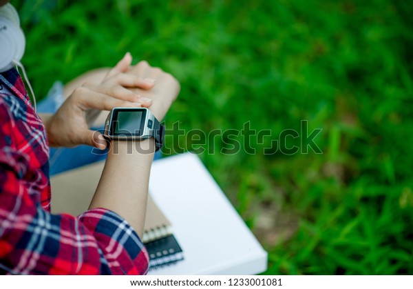 The girl watches the watch in hand, watches the\
time in a black watch, wears a red shirt and a green background.\
And there is a copy space.