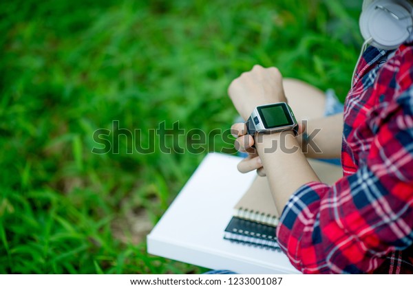 The girl watches the watch in hand, watches the
time in a black watch, wears a red shirt and a green background.
And there is a copy space.