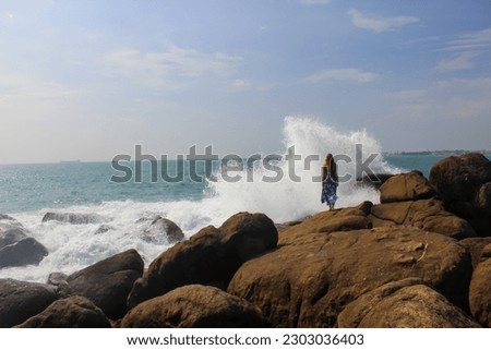 A girl watching beautiful blue waves breaking of big rocks. Stormy weather at sea. Stunning water color at peaceful landscape scene close to Unawatuna beach in southern Sri Lanka