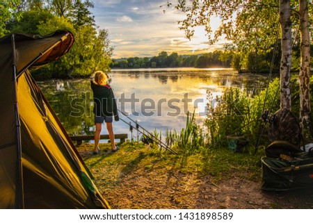 Girl watching sunset while  camping and fishing  by the lake . 