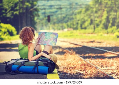 Girl wearing backpack holding map, waiting for a train.