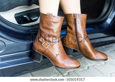 A girl wearing brown leather boots is getting out of a car on the street
