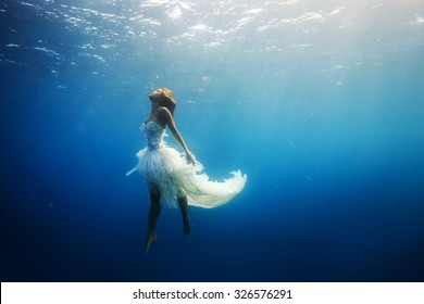 A girl wearing fashion white dress underwater in blue deep. A Wild Ocean Scenery without fish.