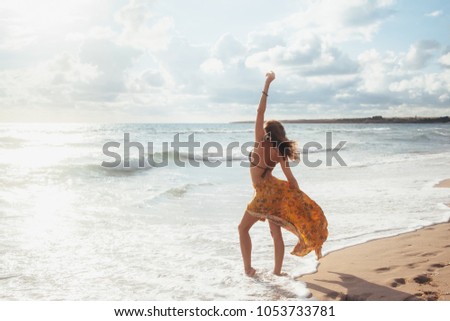 Girl wearing floral maxi skirt walking barefoot on the sea shore. Bohemian clothing style.
