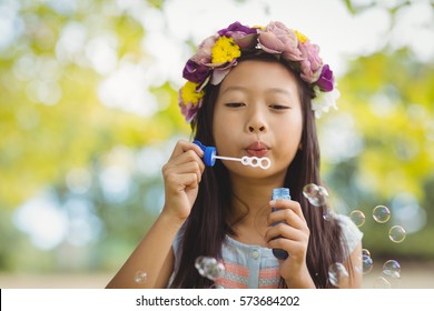 Girl wearing flower wreath blowing bubble wand in park - Powered by Shutterstock