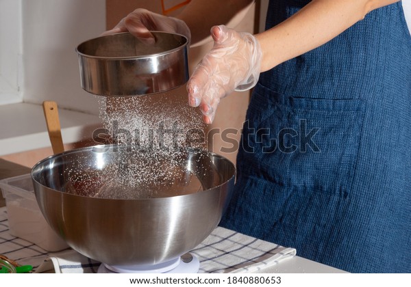 A girl wearing gloves and an apron sifts\
flour through a sieve while making dessert. Getting ready for the\
Day of thanksgiving.