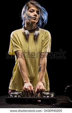 Girl wearing headphones is focused on mixing music on a soundboard. Female DJ with blue hair and yellow t-shirt.