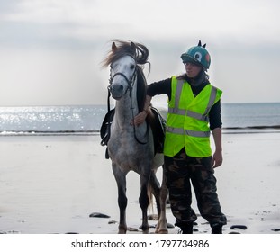 A Girl Wearing Hi Vis Next To Her Stallion On The Beach