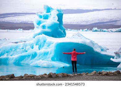 A girl wearing an Icelandic wool cap admires the unique blue icebergs on Lake Jökulsárlón, a unique glacial lake at the Vatnajökull glacier	 - Shutterstock ID 2341548573