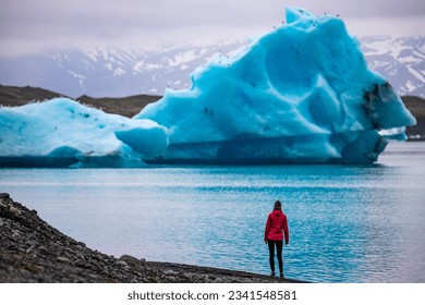A girl wearing an Icelandic wool cap admires the unique blue icebergs on Lake Jökulsárlón, a unique glacial lake at the Vatnajökull glacier	 - Shutterstock ID 2341548581
