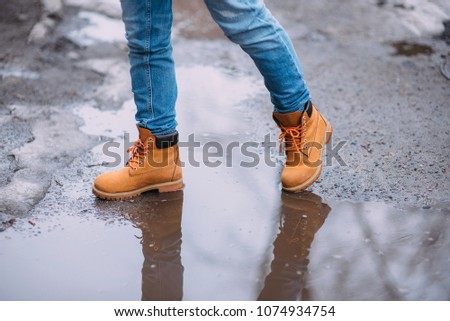 Girl wearing jeans and yellow boots splashing in a puddle after rain