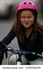Girl Wearing A Pink Helmet Riding Her Bike While Making A Goofy Face.