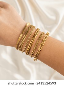 Girl wearing set of gold chain bracelets on wrist with silky fabric background