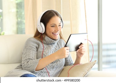 Girl Wearing Sweater Listening Music On Line With A Tablet Sitting On A Sofa In The Living Room At Home In Winter