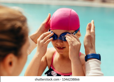 Girl wearing swimming goggles by poolside with female coach in front. Girl getting ready for her swimming class. - Powered by Shutterstock