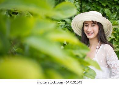 A Girl Wearing A White Hat Stands Smiling Happily Behind A Bush On The Beach.close-up