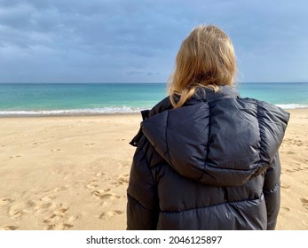 Girl Wearing A Winter Coat Standing On A Sandy Beach