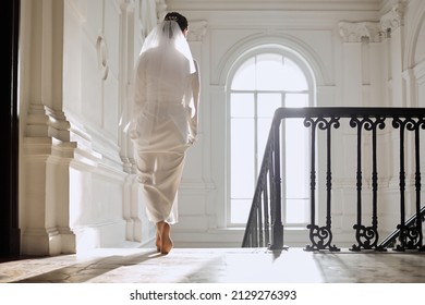 A girl in a wedding dress walks barefoot in a bright hall