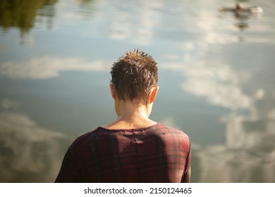A girl in wet clothes sits by the lake. A woman is resting in the summer on the pier. After swimming in the countryside. Woman with short hair.