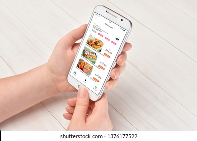 Girl While Sitting At The Table Ordering Food On Her Smartphone With Food Delivery App