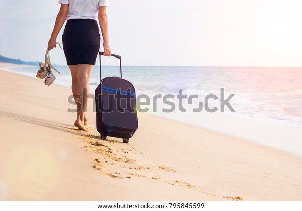 Girl in a\
white blouse and black skirt in office clothes clerk manager goes\
away walk on the beach on the sea and sand background with a\
suitcase on wheels luggage. Go for weekend.\
