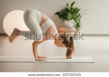 A girl in white clothes does a handstand on a mat indoors.