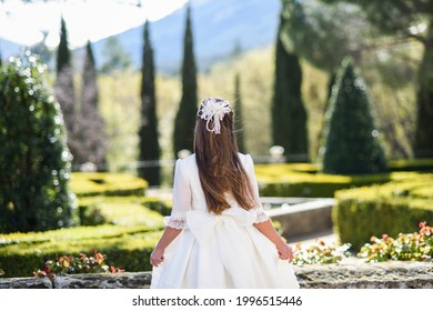 Girl in white communion dress with bow on her back in a park for a photograph - Shutterstock ID 1996515446