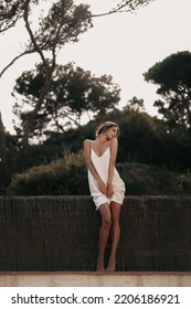 
Girl In A White Cotton Dress In Nature Near The Fence. Natural Appearance Without Nude Makeup. Spain Landscape. Beautiful Girl Posing