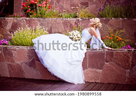A girl in a white dress with a bouquet of flowers sits on the stones. Blonde bride with flowers