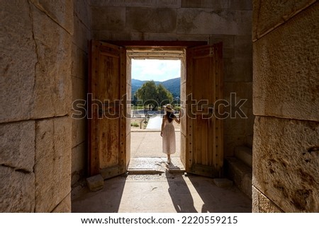Girl with white dress and hat is posing at the door of Patara Assembly Hall (aka Patara Meclis Binası) against morning  sun. Patara Ancient City, Antalya, Turkey