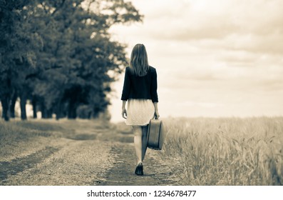 girl in white dress and jacket with suitcase at countryside road near wheat field. Image in black and white color style - Shutterstock ID 1234678477