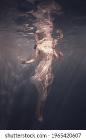 A girl in a white dress with long dark hair swims underwater as if floating in weightlessness