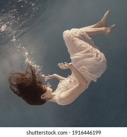 A Girl In A White Dress Posing And Somersaulting Under Water As If Flying In Zero Gravity