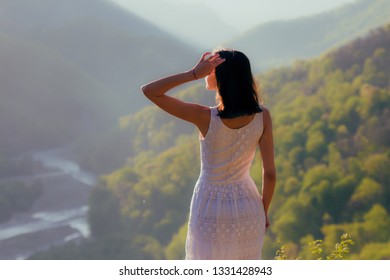 Girl in white dress standing back the top Caucasus mountain and scenery view to sunset at green valley and river  Female travel nature concept 