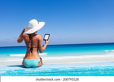 Girl with white hat reads kindle on beach - Powered by Shutterstock