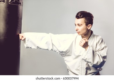 Girl In A White Kimono Beats Black Punching Bag Isolated On Grey Background. Of Tae Kwon Do, Karate, Kick