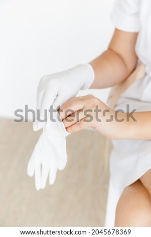 a girl in a white lab coat is wearing a white rubber medical glove. the room is on a white background. The concept of cosmetology and medical services.