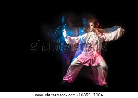 Girl in a white and pink wear engaged wushu against a dark background with slowspeed technic.