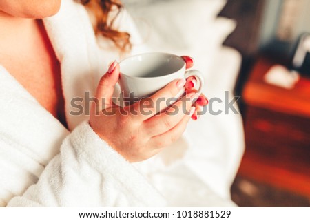 Girl in a white robe holding a white mug of coffee in his hands. Coffee in bed. The morning starts with coffee. Stylishly toned photo
