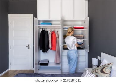 A girl in a white shirt and jeans puts clothes in a closet, puts things in order - Shutterstock ID 2178184011